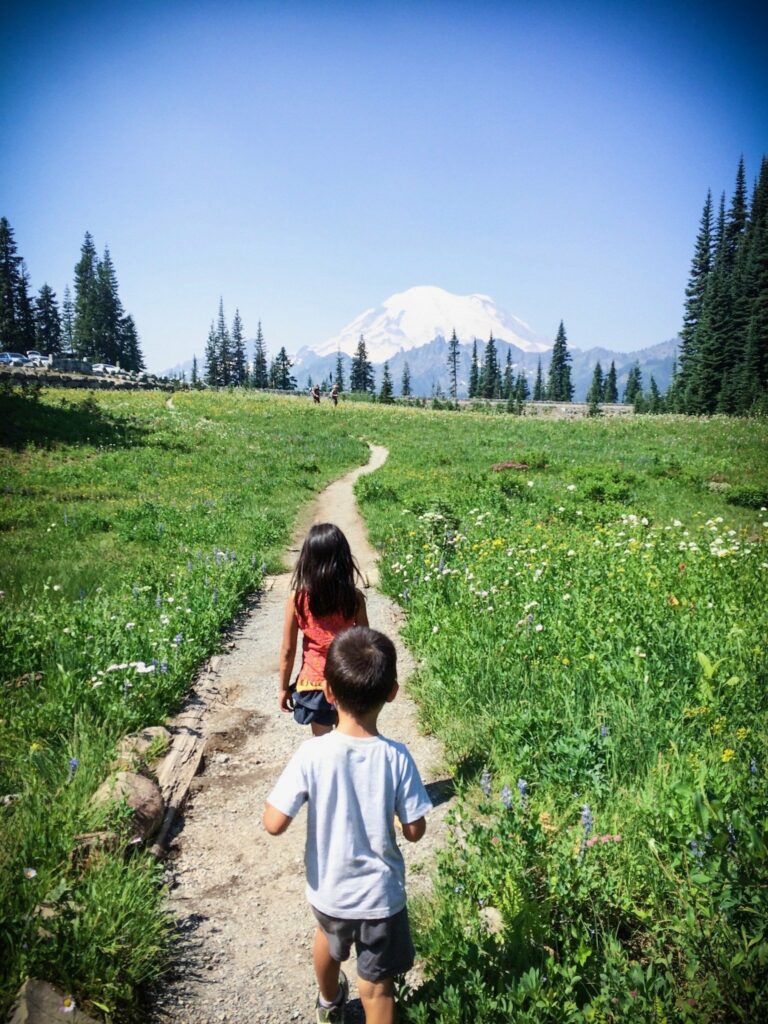 A girl and a boy taking Mount Rainier hikes along a trail with Mount Rainier in the distance
