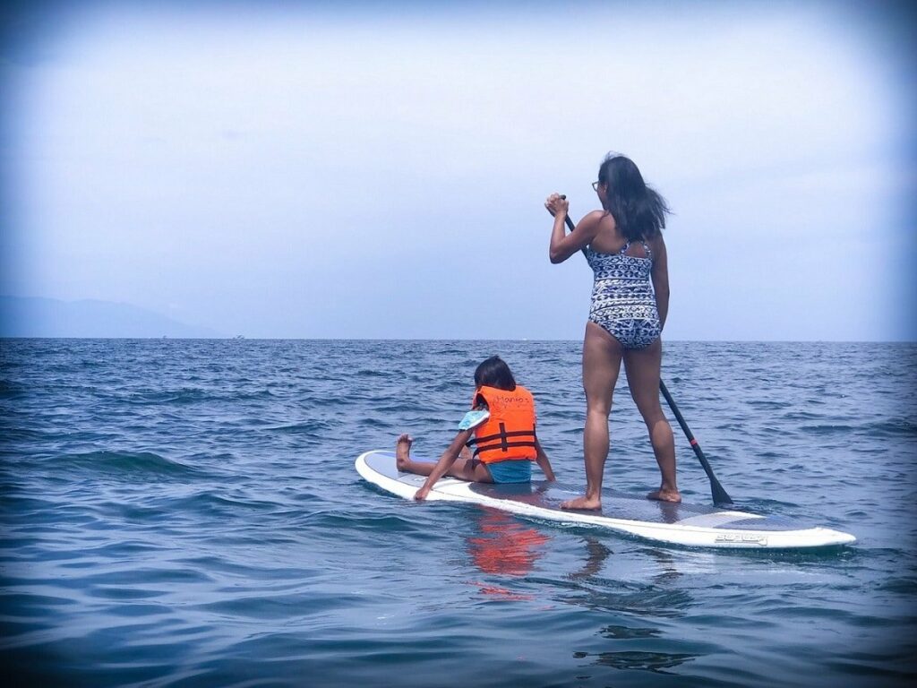 A mother and daughter paddle boarding and doing travel fitness