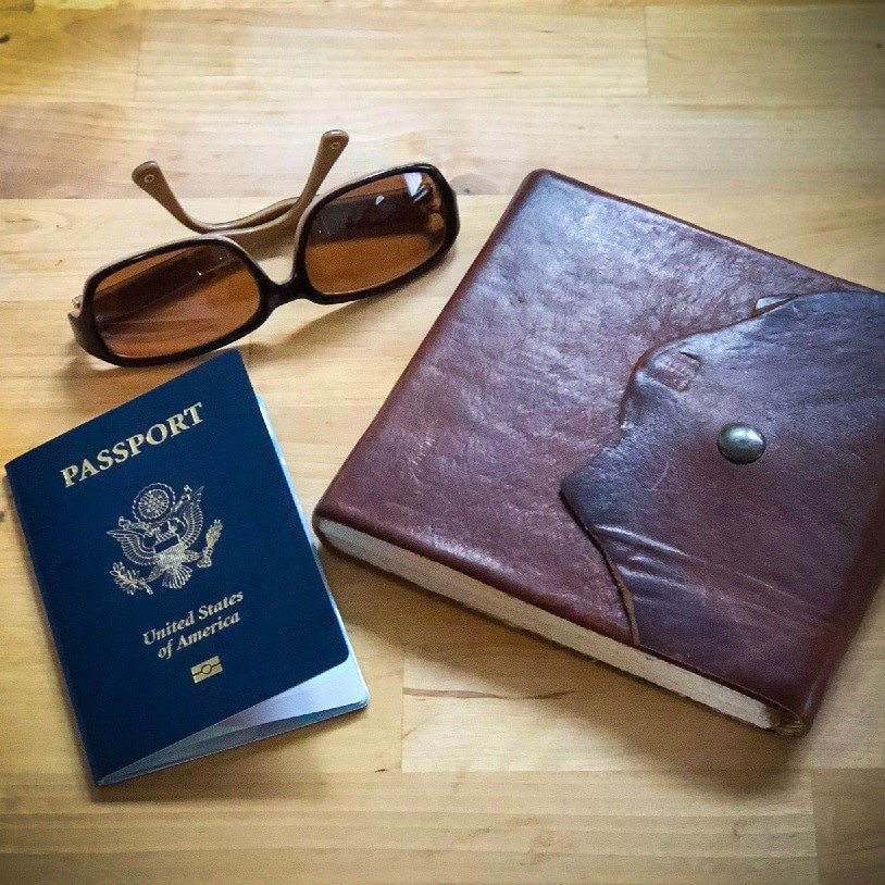 A pair of fashion sunglasses, a USA passport, and a leather-bound journal on a wooden counter for responsible travel.
