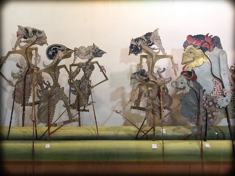 Seven Indonesian shadow puppets from the island of Java, displayed on a bamboo log at the Sonobudoyo Museum in Yogyakarta, where travelers can learn Indonesian.