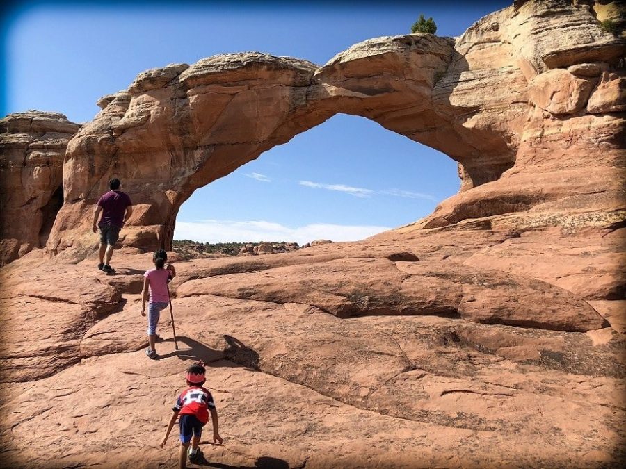 A man, a girl, and a boy hiking near a natural arch at Arches National Park and practice responsible travel