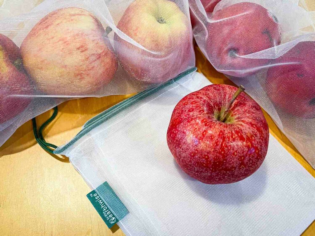 Mesh produce bags with red apples in them on top of a table, eco friendly travel products.