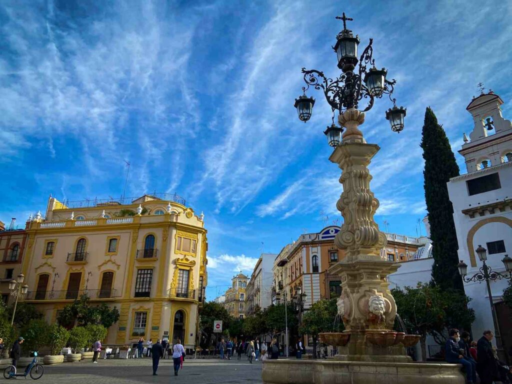 A square in Seville, with a fountain in the foreground and a yellow colonial building in the background