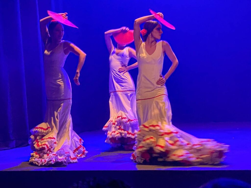 Three flamenco dancers in white and red dresses and holding red fans