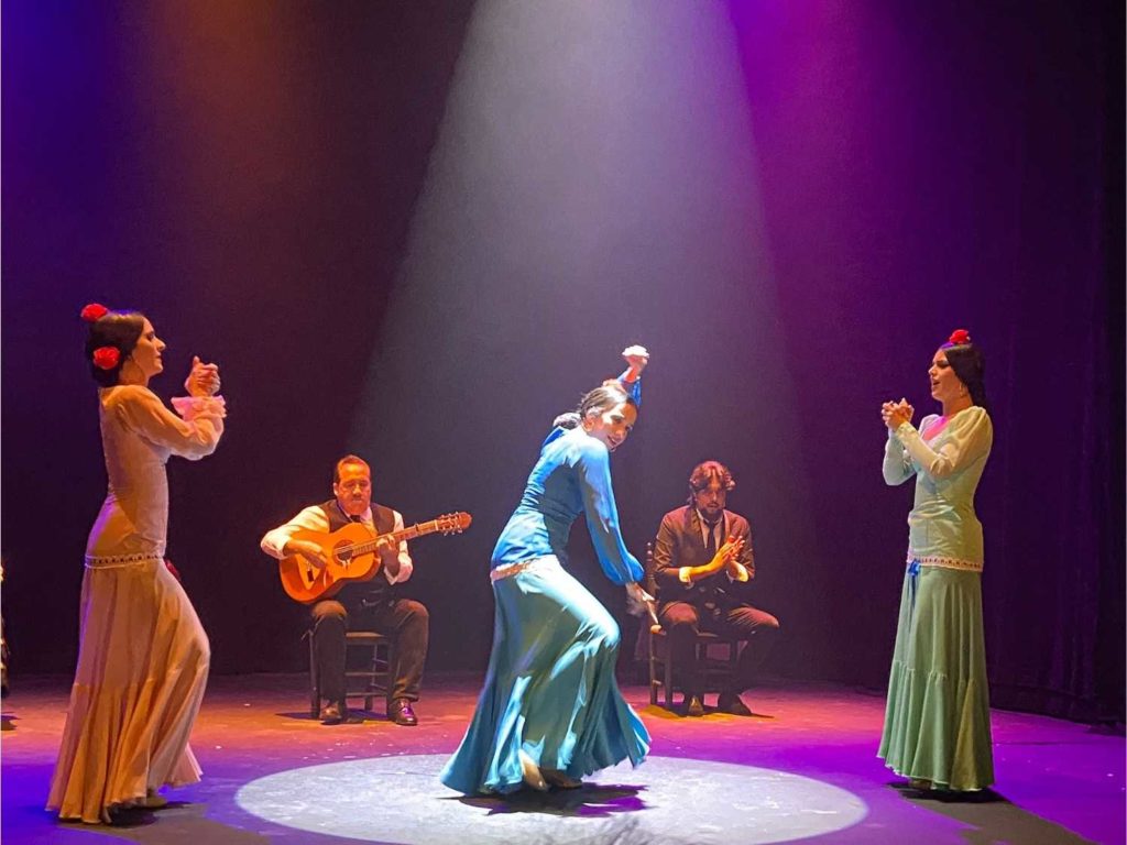 Flamenco dancers performing on a stage with a flamenco guitarist and singer in the background
