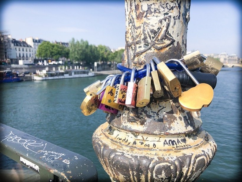 Pont des Arts during a Paris 3 day itinerary. A view of padlocks on a bike chain, around one of the posts on the bridge in the foreground. In the background is the River Seine.