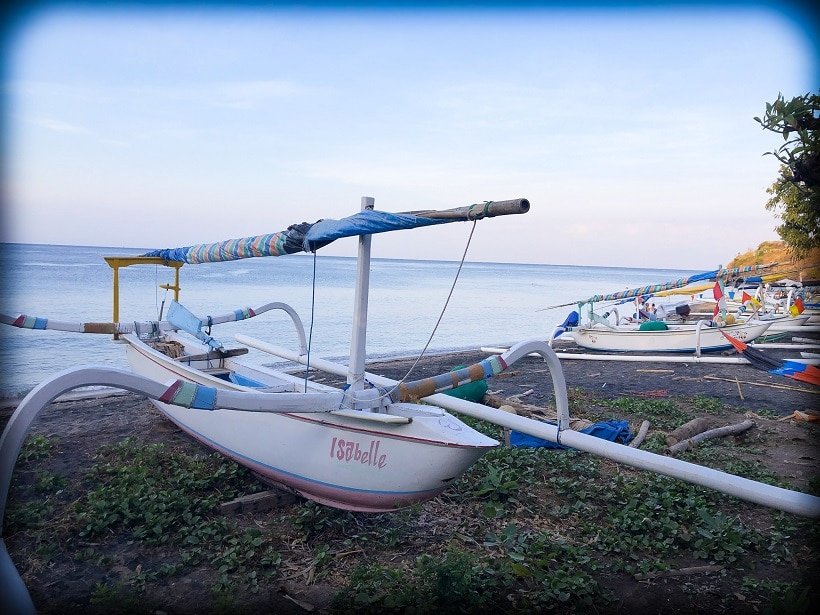 A traditional Balinese fishing boat with bamboo outriggers sits on the beach in Amed Bali