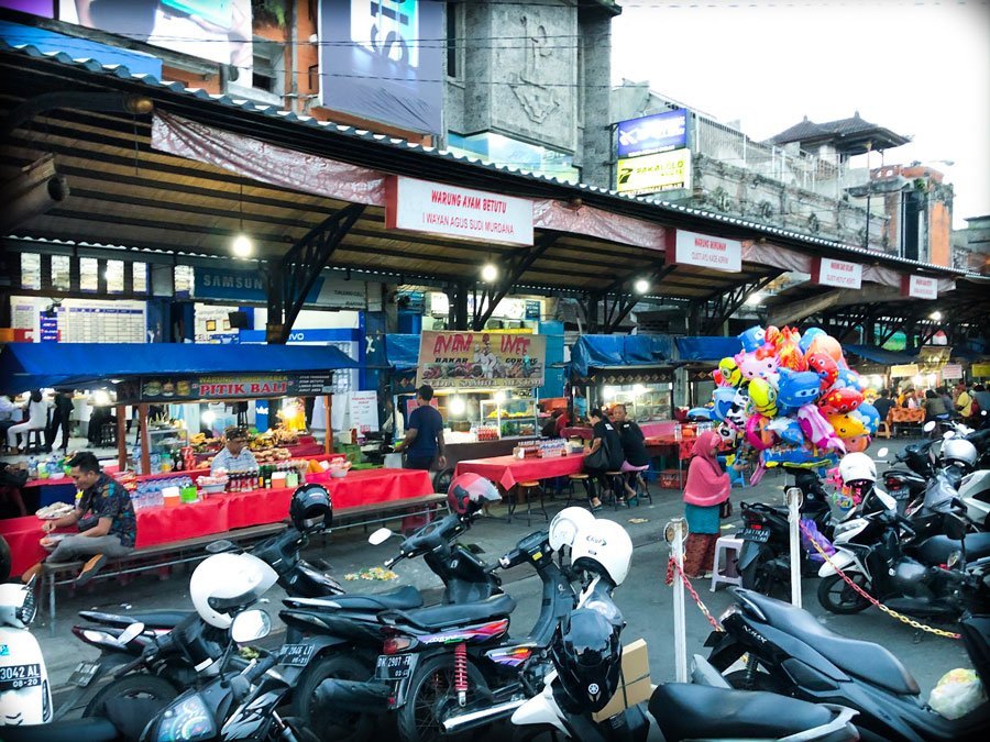 Food stalls with motorcycles parked in front at a Bali night market in Gianyar, Indonesia. 
