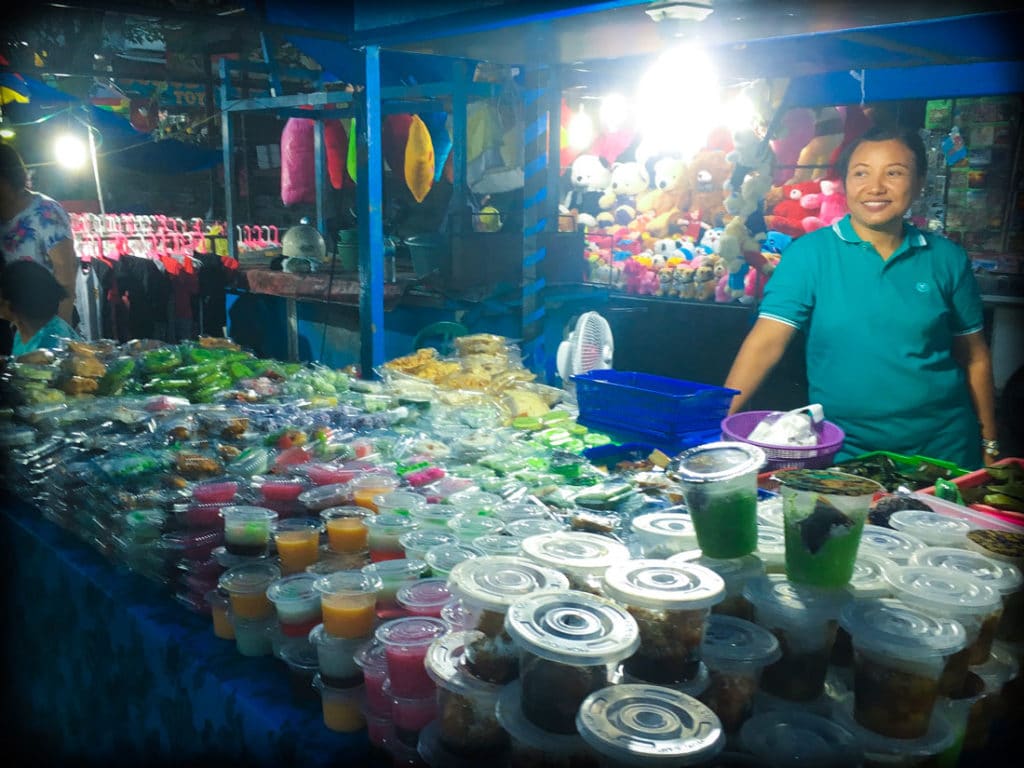 A food vendor at a Bali night market in Gianyar, Indonesia selling jellies in plastic cups and sweet treats in plastic containers