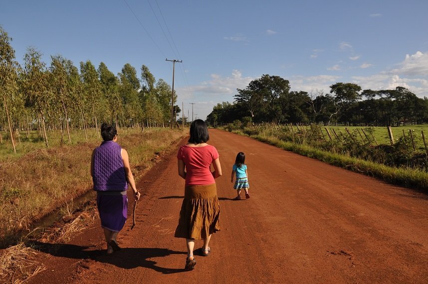 Women walking along a red dirt road in Paraguay, following a girl. 