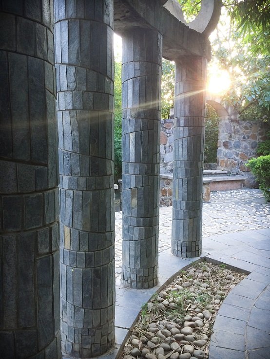 A sun flare behind stone columns at Garden of Five Senses in Delhi, India, where families can go during a visit to Delhi with kids