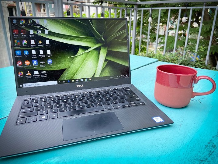 A laptop used by a worldschooling family and a cup, sitting on a blue table outdoors