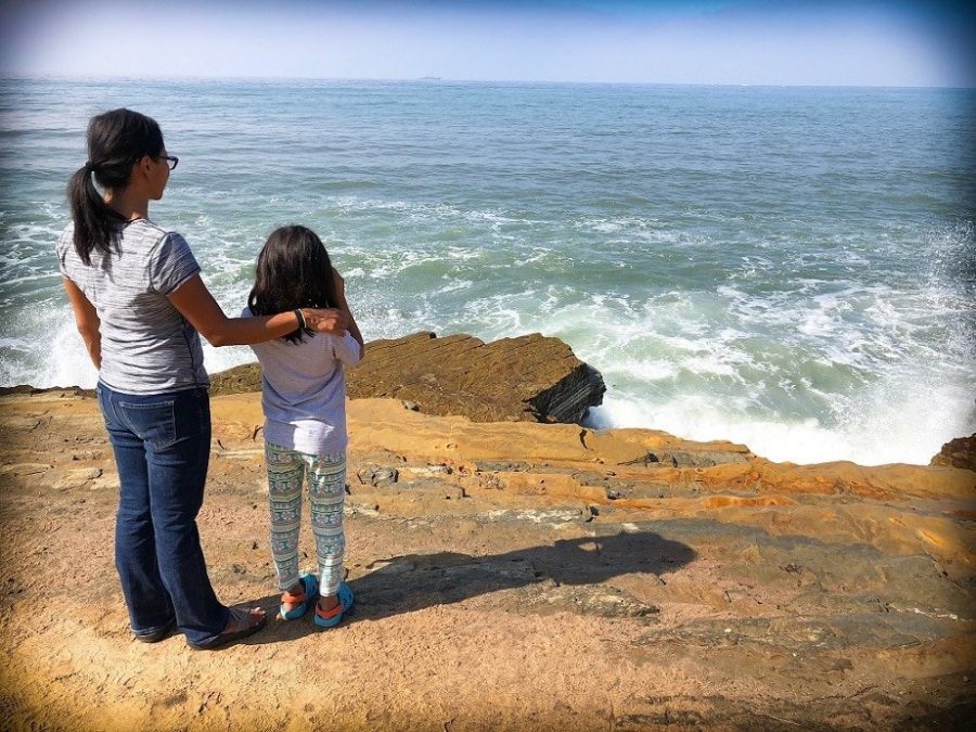Mom and daughter of a worldschooling family standing on edge of a cliff looking out into the ocean.