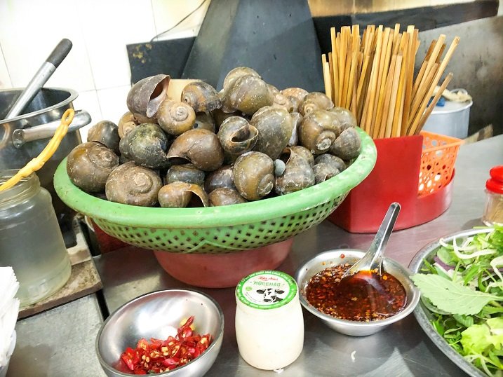 Snail shells in a basket on a metal counter serving food in Hanoi.