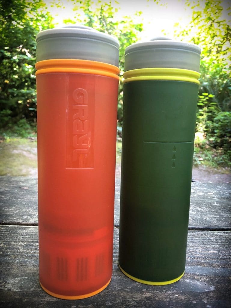 An orange GRAYL portable water filter for travel next to a green GRAYL water bottle on a wooden table
