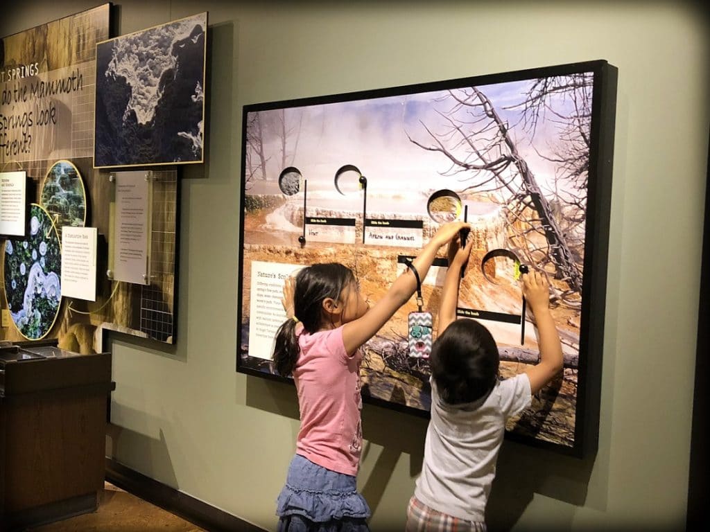 A girl and a boy from a world schooling family interacting with an exhibit at the visitors center at Yellowstone National Park