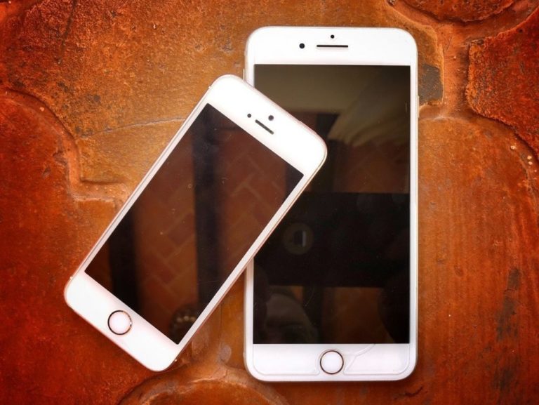 Two white Apple smart phones on a brick floor that uses a travel WiFi router - the one on the left is smaller than the one on the right, and is leaning on the larger phone at an angle.