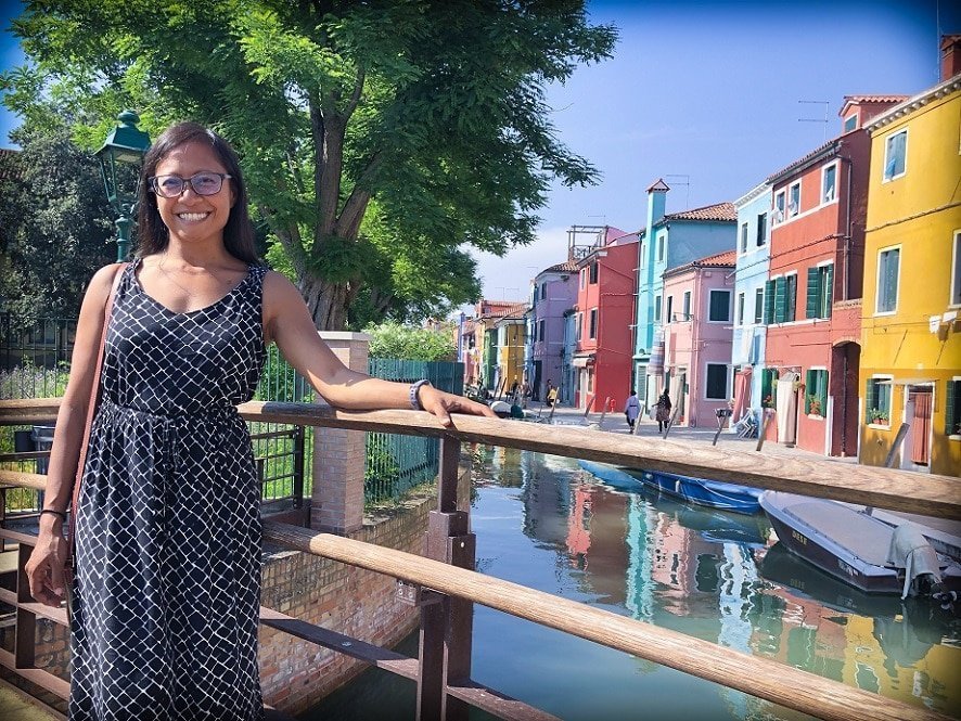 A woman standing next to a canal and colorful buildings in Venice during an Italy itinerary
