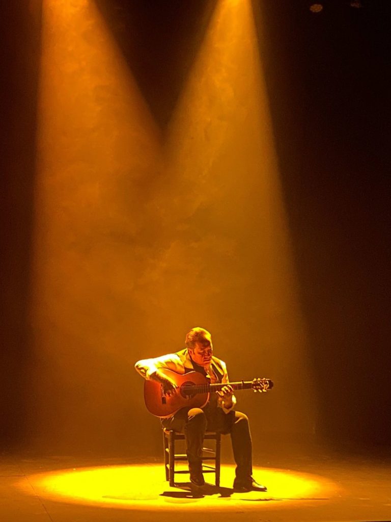 A Flamenco guitarist on a stage with the spotlight