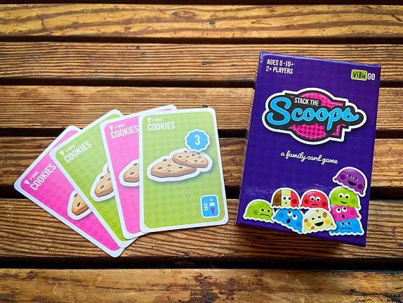 A set of playing cards and a box called Stack The Scoops on a wood background, used as family-friendly worldschooling resources