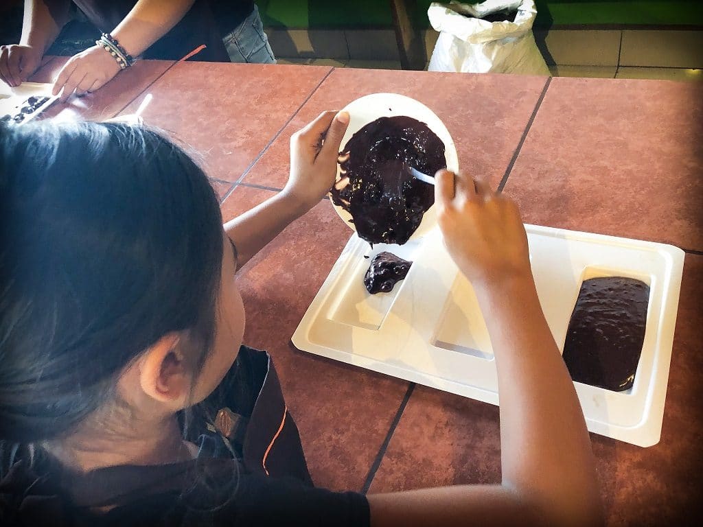 A girl pours chocolate ganache into a mold during a chocolate workshop at ChocoMuseo La Fortuna