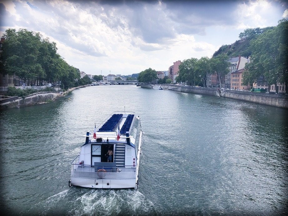 A view of the Saone River in Lyon, France, with a boat on the river in the foreground. Boat cruises are one of the things to do in Lyon.