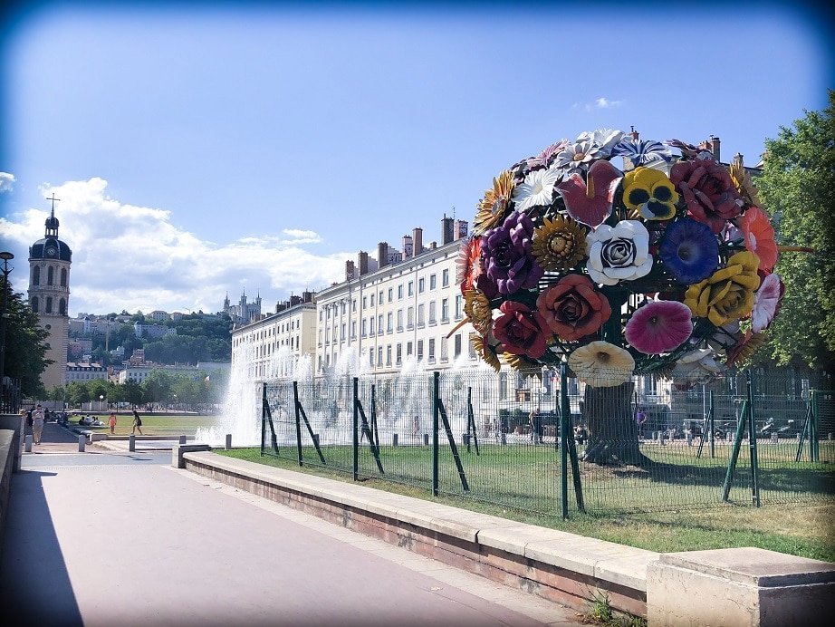 A street view of Lyon, France, with a large sculpture of a bouquet of flowers, the size of a tree on the right side of the picture.